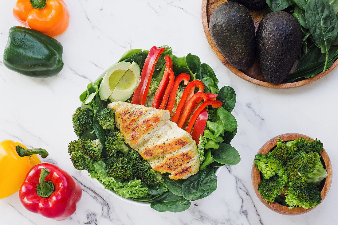 Roasted chicken with broccoli, red pepper and halved avocado on a bed of green leaves