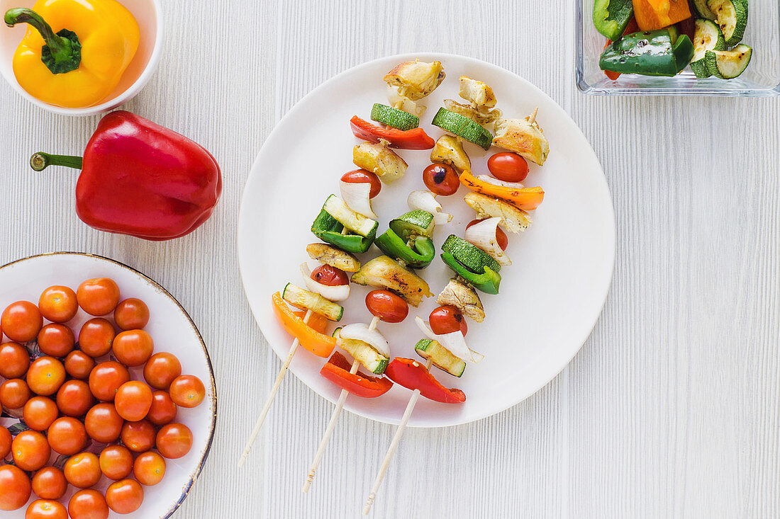 Chicken skewers with pepper placed on plate near cherry tomatoes and roasted zucchini