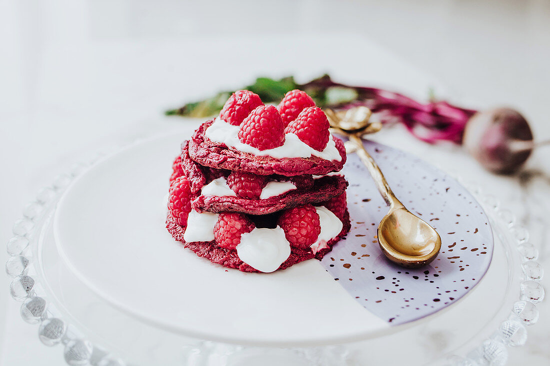 Organic beet pancakes with fresh raspberry on plate with golden spoon on white table