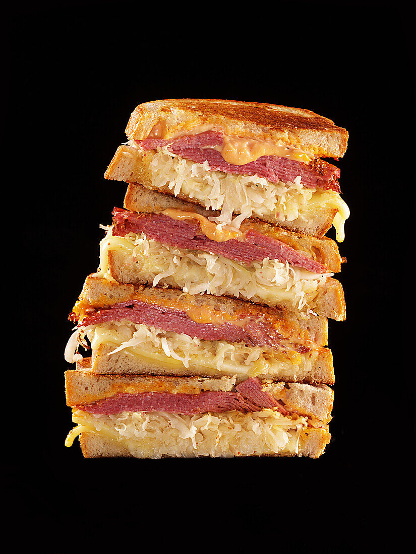 Several Reuben sandwiches stacked against a black background