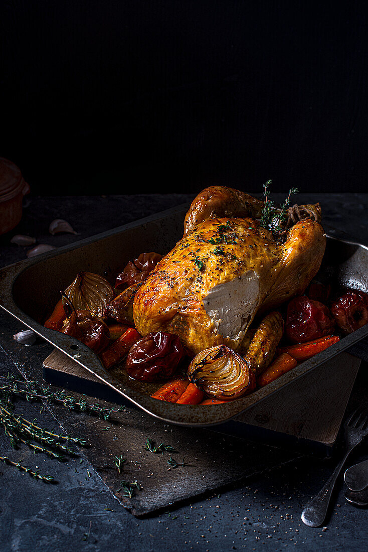 Roast chicken with roasted onions, apples and carrots in a roasting tin