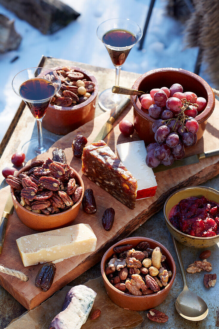 Käseplatte mit Weintrauben und Knabbernüssen auf Holztisch im verschneiten Garten