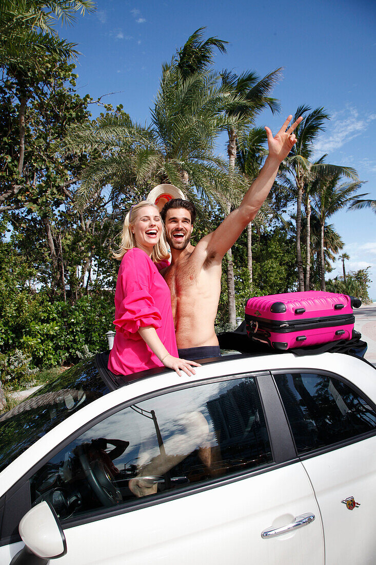 Cheerful couple in holiday spirit are standing in the roof window opening of a car