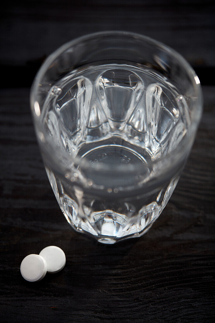 Zwei Aspirin-Tabletten neben einem Glas Wasser