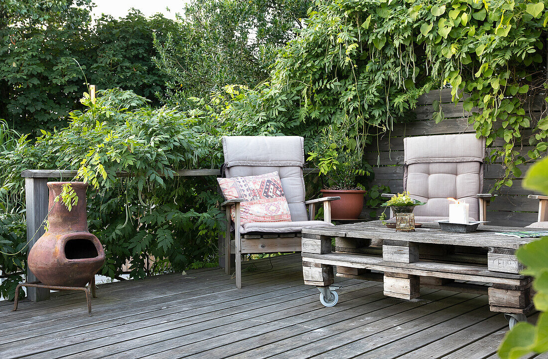 Pallet table, chairs and small fireplace on wooden deck overgrown with wisteria and morning glory