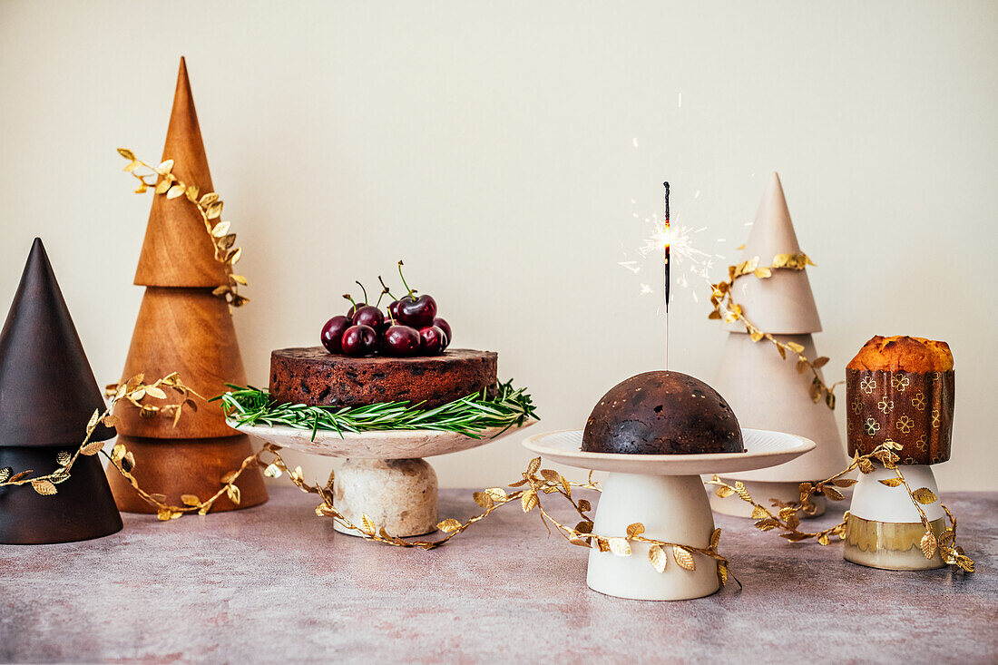 Fruit Cake, Christmas Pudding with Sparkler and Pannetone in setting with Wooden Christmas Trees