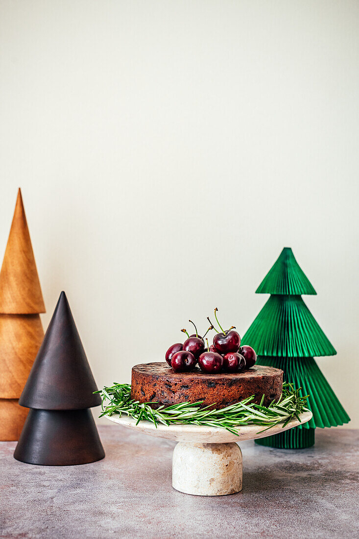 Früchtekuchen mit Kirschen daneben dekorative Weihnachtsbäume aus Holz und Papier