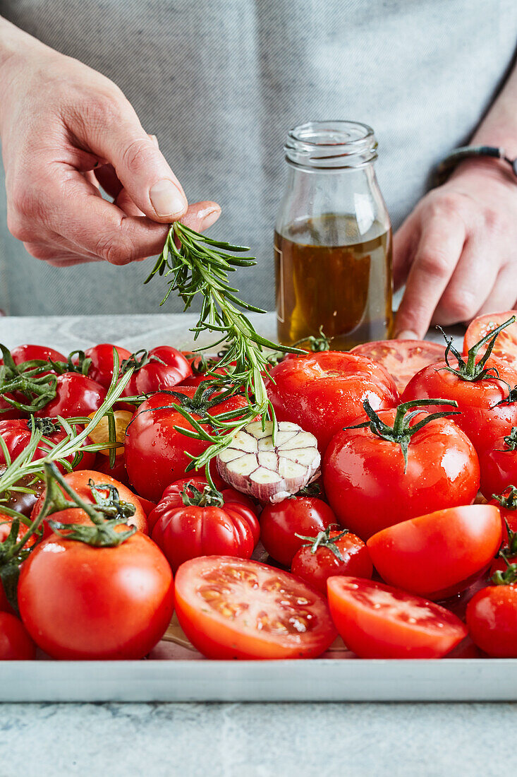 Geröstete Tomatensauce aus dem Ofen zubereiten - Kräuter, Knoblauch und Öl dazugeben