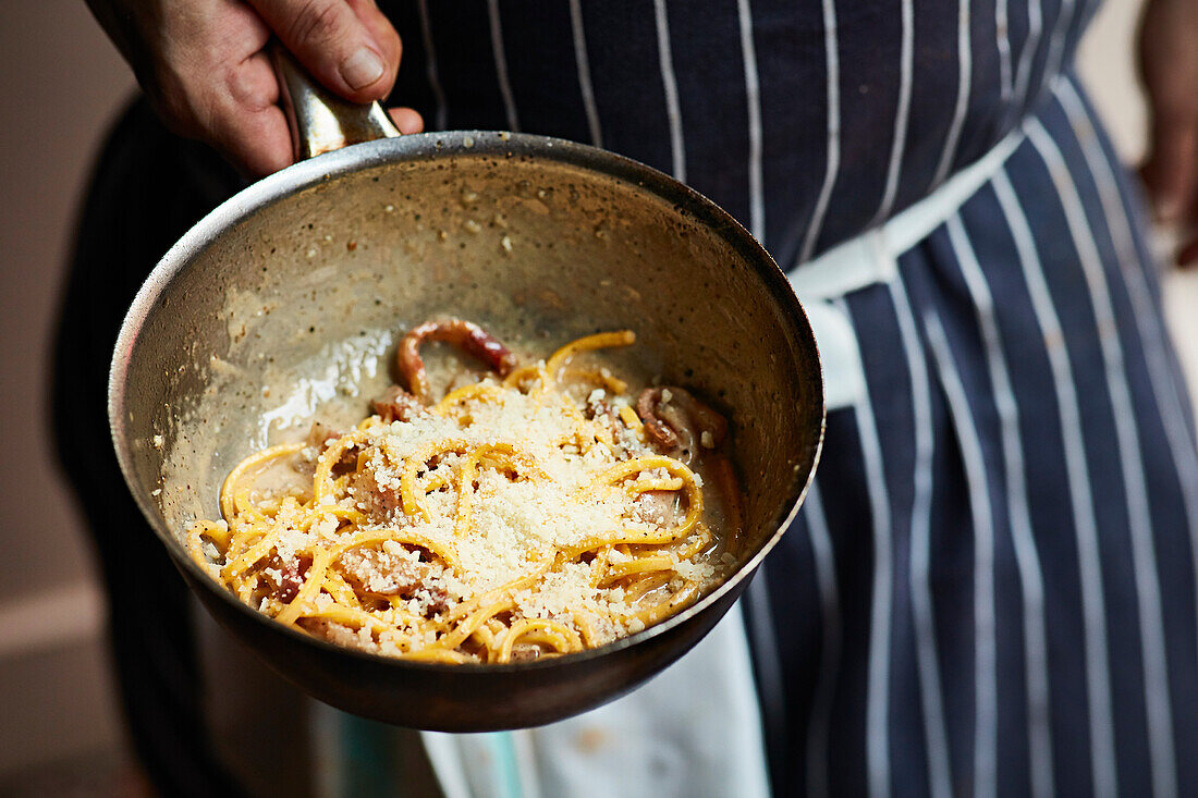 A chef serving pasta with Parmesan from a pot