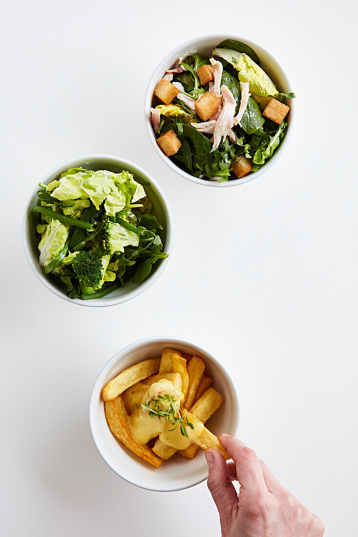 Three different side dishes: mixed leaf salad with chickeny and croutons, mixed leaf salad with vegetables, and French fries