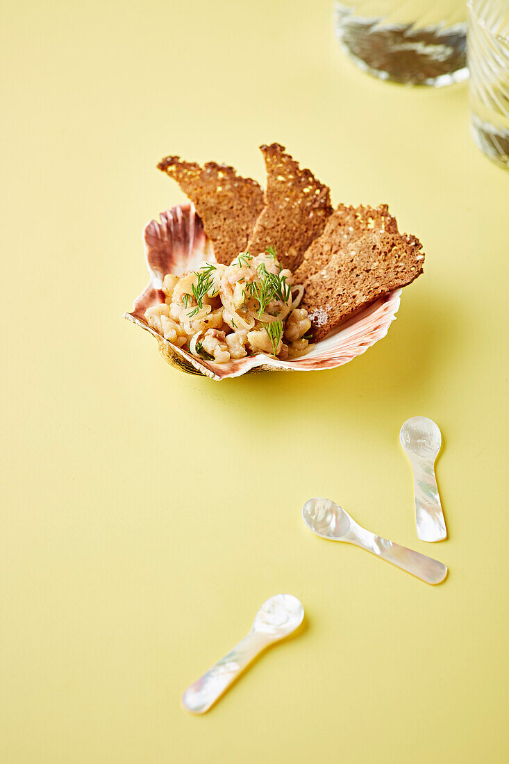 Meeresfrüchtesalat mit Knäckebrot serviert in großer Muschelschale mit Perlmutt-Löffeln