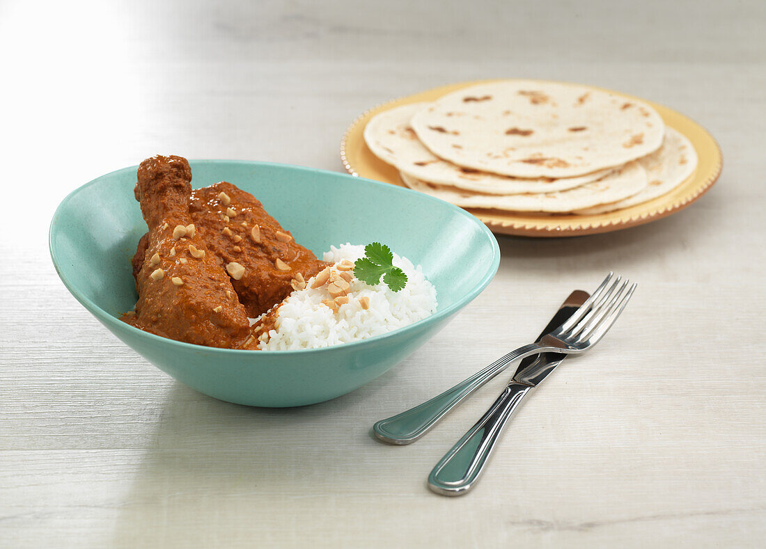 Hähnchen in Erdnusssauce serviert mit Reis und Fladenbrot