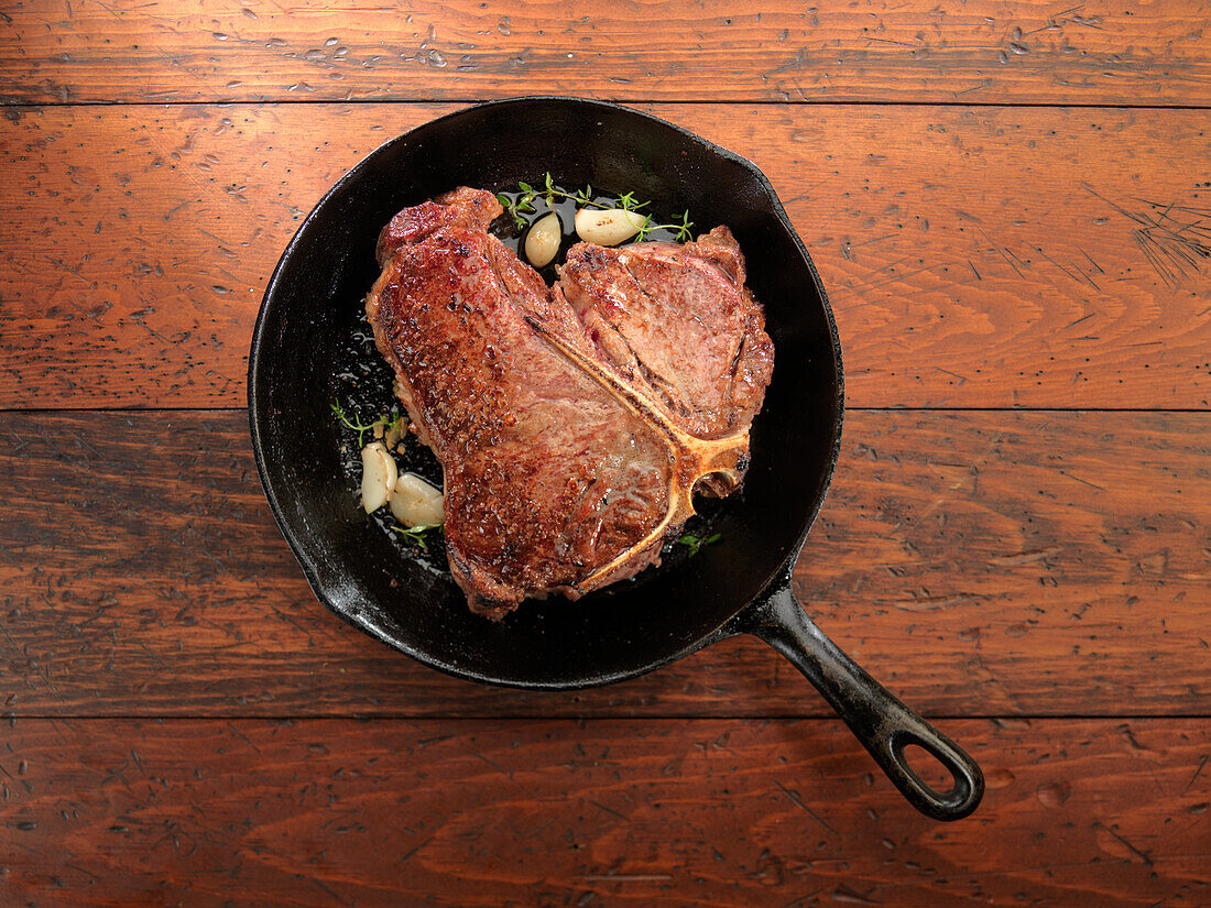 A Porterhouse steak with garlic and rosemary in a pan
