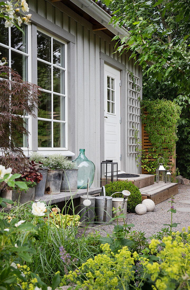 Zinc pots, balloon bottle, and watering cans in front of the guest house with gravel terrace