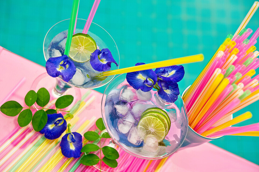 Drinks with ice cubes, limes, straws and flowers by the pool