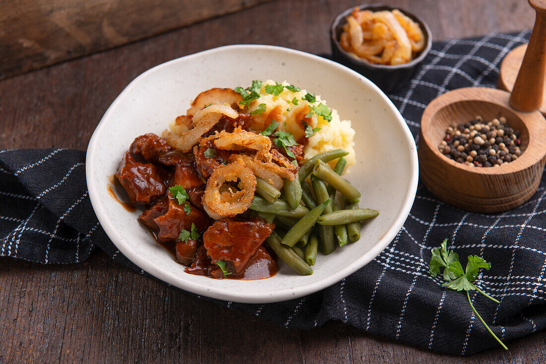 Kartoffelstampf mit grünen Bohnen, Seitan-Gulasch und gebratenen Zwiebelringen, vegan