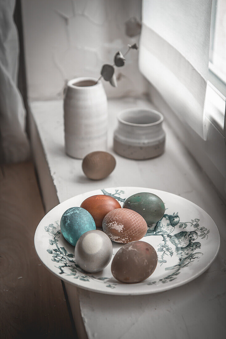 Teller mit gefärbten Eiern auf Fensterbank