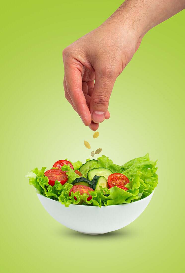 Bowl of salad with cucumbers, tomatoes, iceberg salad leaves, pouring oil over salad