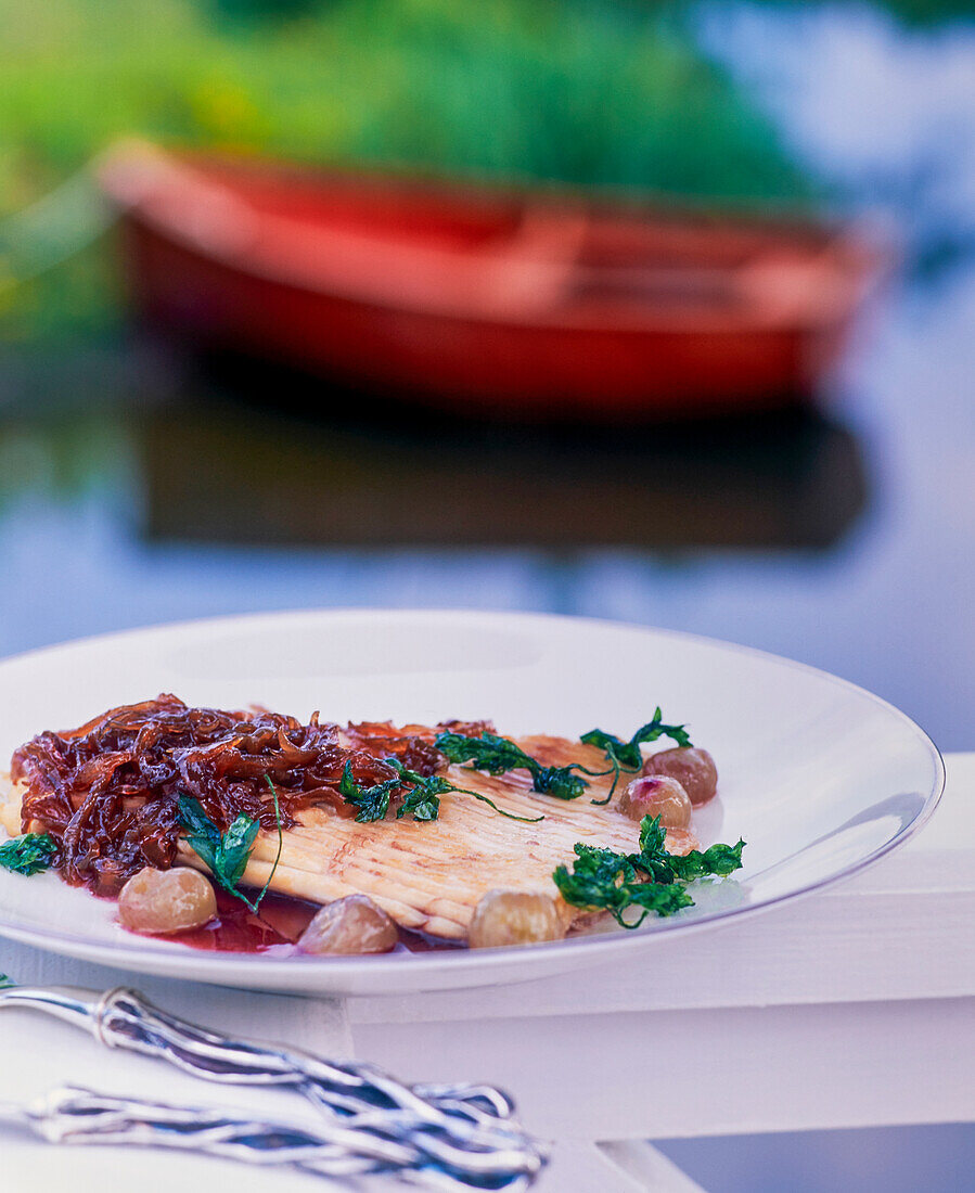 Rochen mit Trauben und Zwiebel-Confit auf Holzbrüstung am See