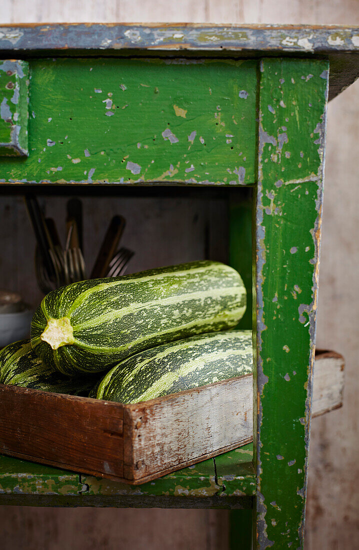Fresh zucchini in a wooden crate under a green wooden table