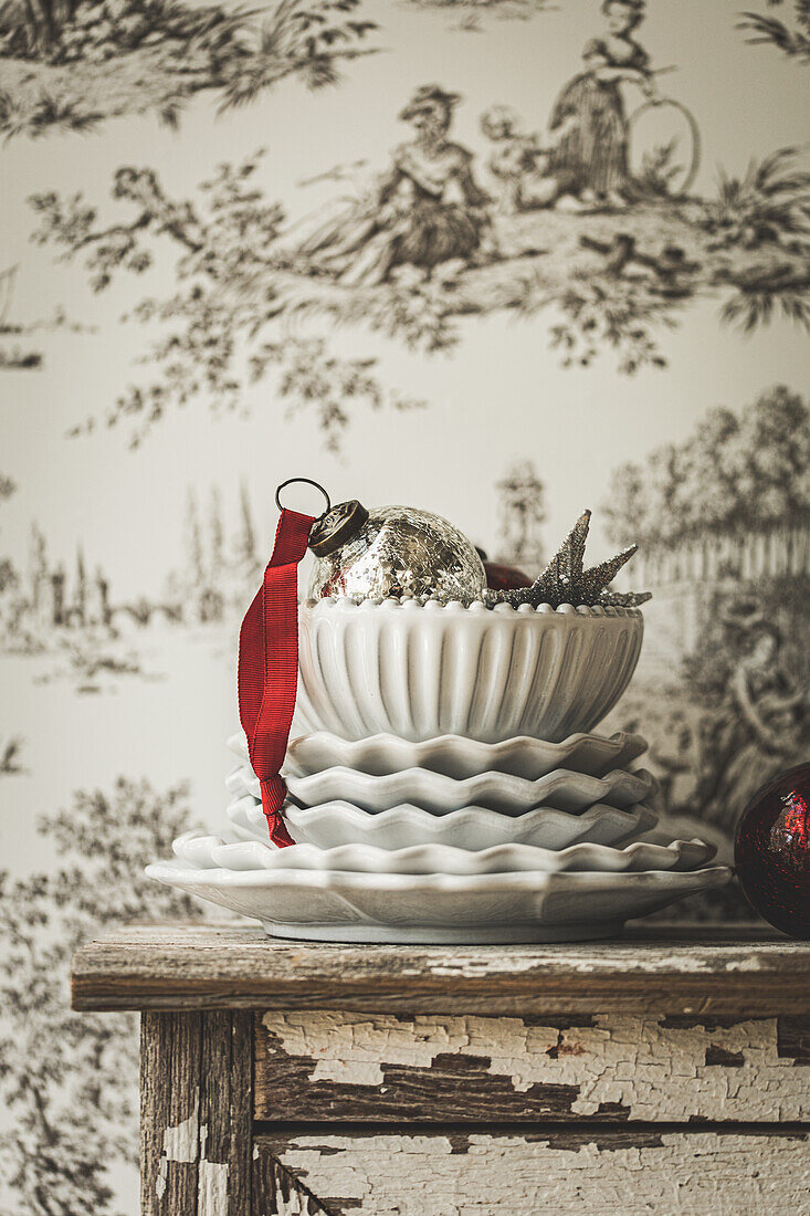 Stack of plates and sleeping bags with Christmas decorations in front of Toile de jouy wallpaper