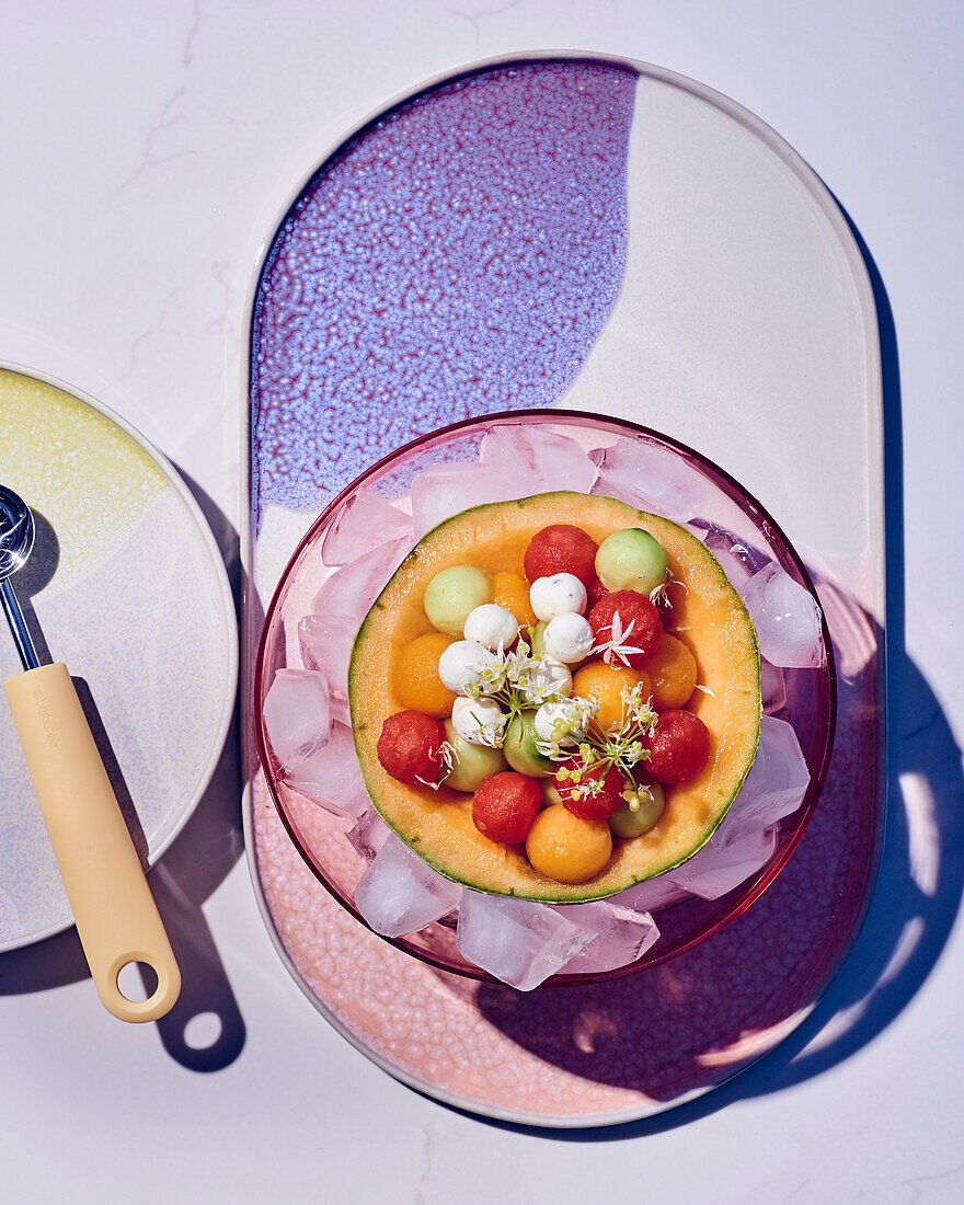 Colorful melon and cucumber balls with goat cheese served in a hollowed melon shell