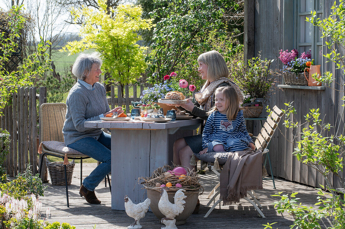 Frauen und Kind beim Osterfrühstück am gedeckten Tisch auf der Terrasse