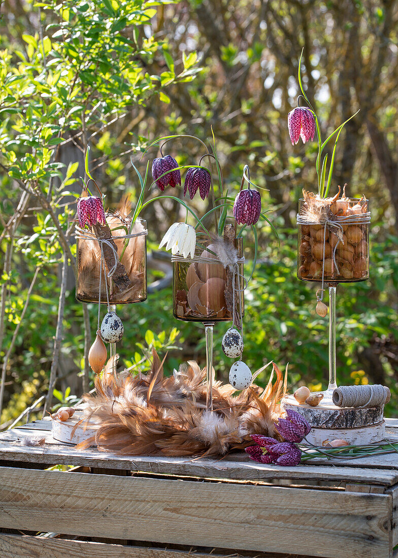 Vases filled with bulbs, checkerboard flowers (Fritillaria), eggs and feathers as Easter decoration on wooden table in the garden