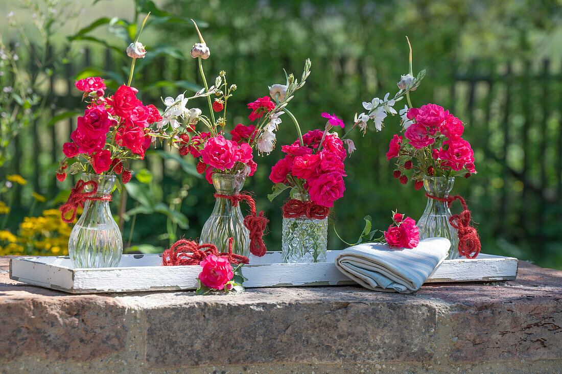 Bouquets of roses, candles and bulbs in glass vases on a wooden tray