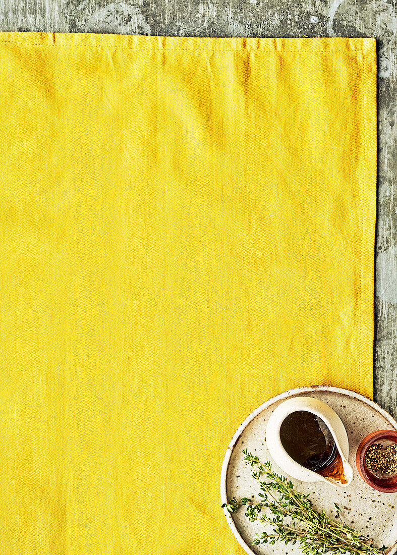 Yellow fabric background, tray with sauce and herbs