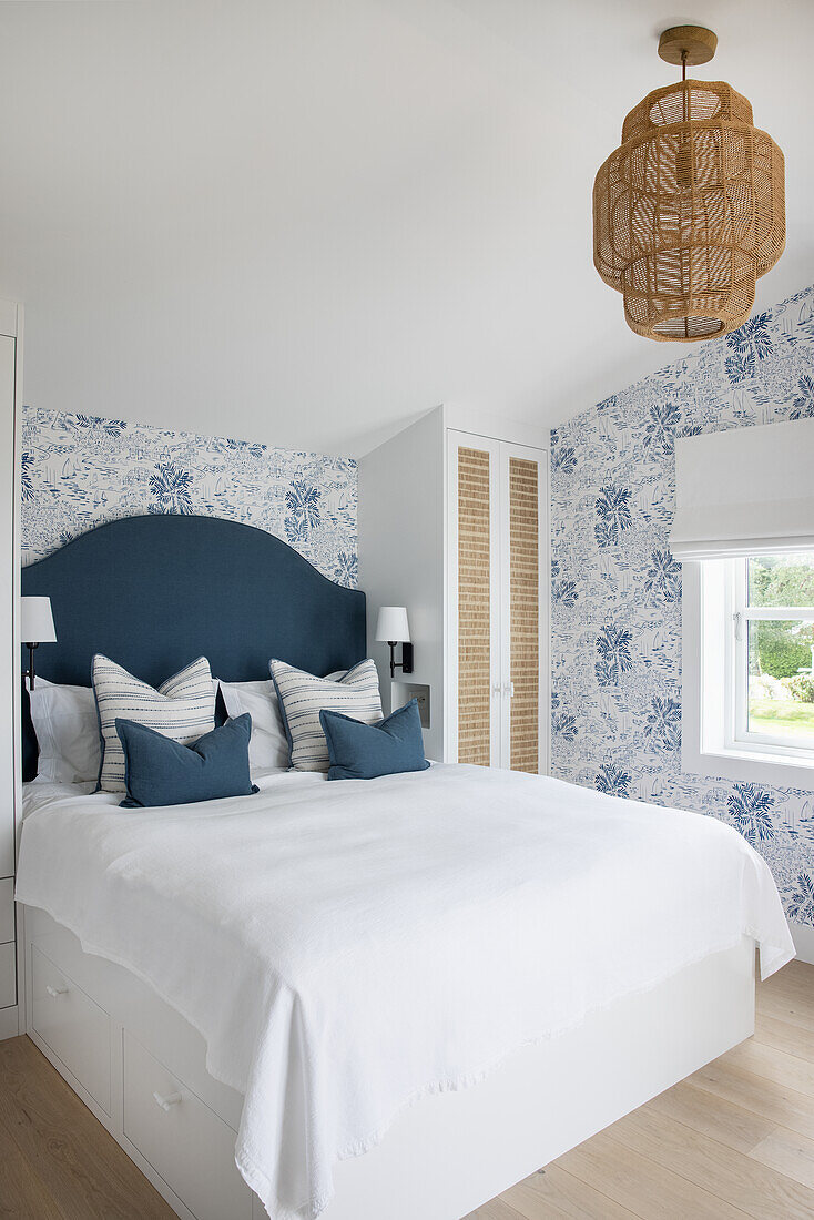 Double bed in bright, light-flooded bedroom with blue and white wallpaper