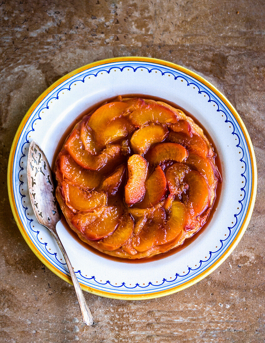 Peach tarte tatin on a plate with silver pie server