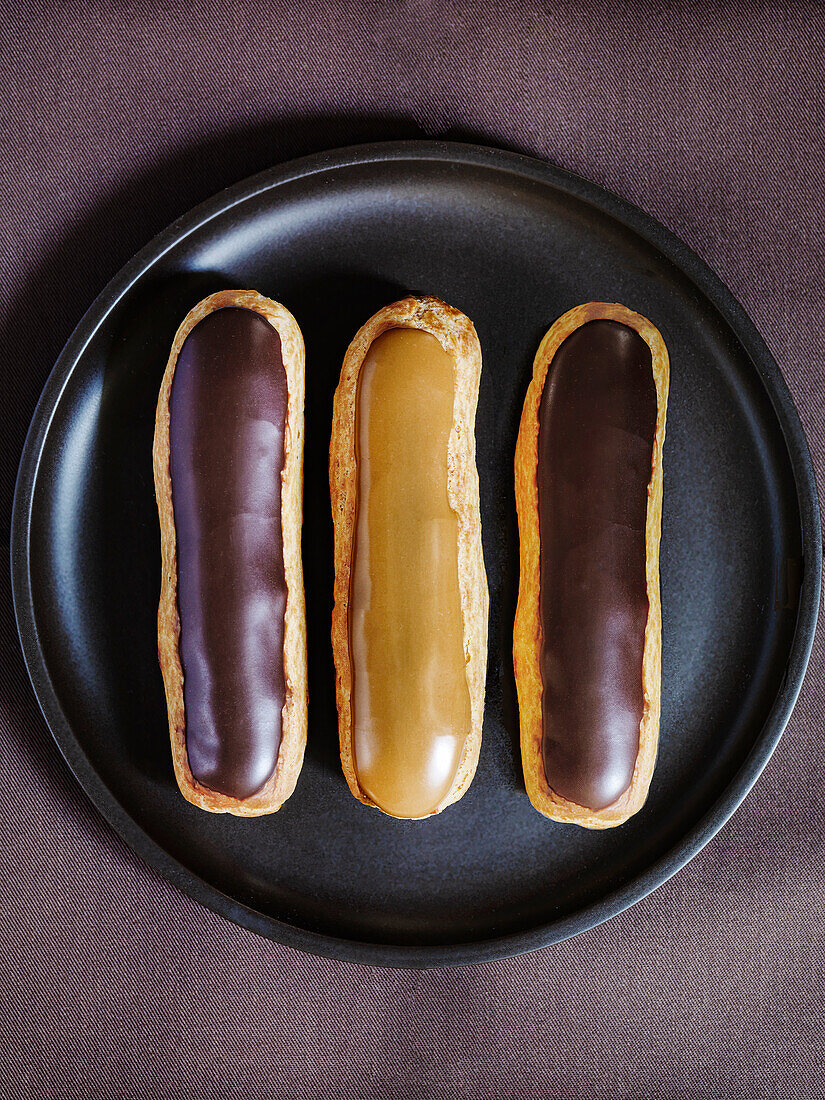 Eclairs with chocolate and caramel icing on a black plate