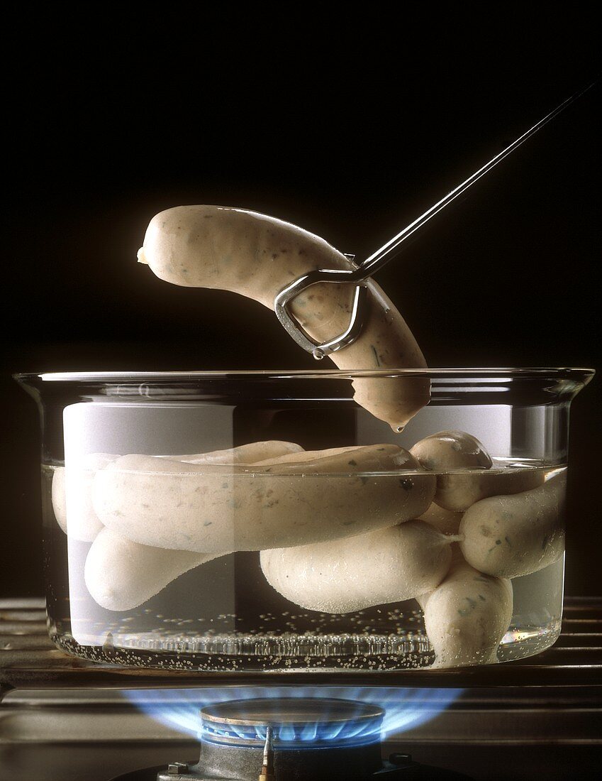 White sausages (Weisswursts) cooking in glass pan on stove