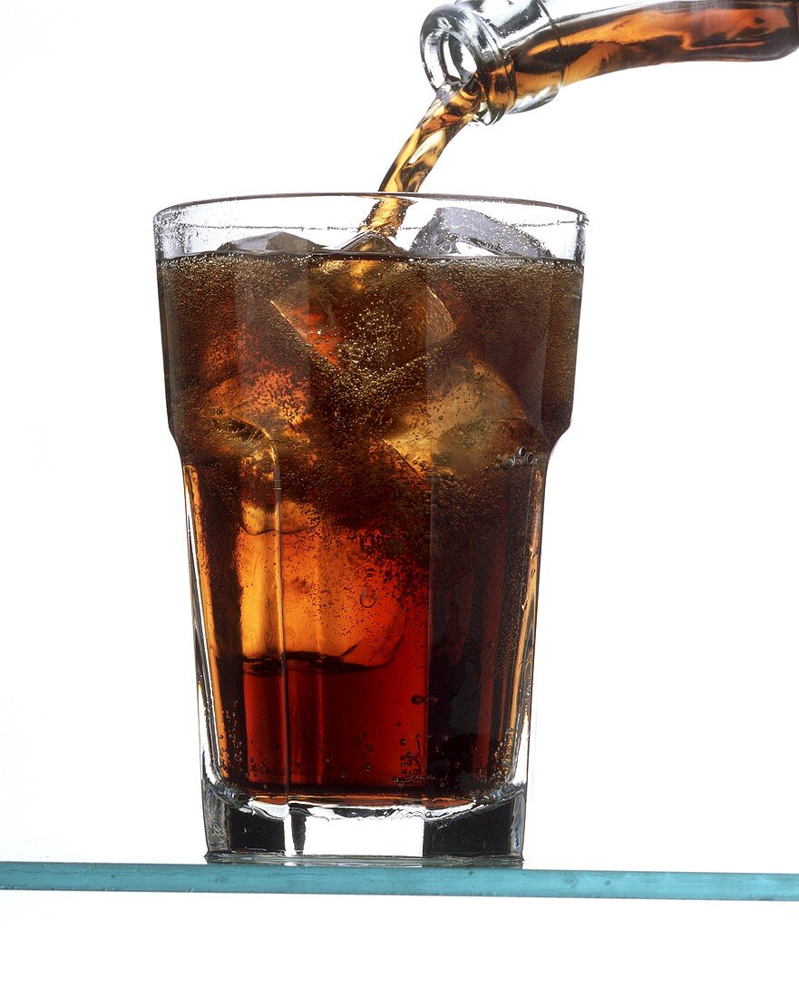 Pouring cola into a glass with ice cubes (glass almost full)