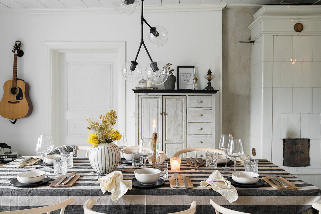 Cosy dining room with set table, grey tiled stove, guitar on the wall