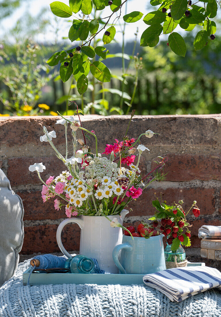 Summer bouquet and pitcher of strawberries on ground cushion in garden