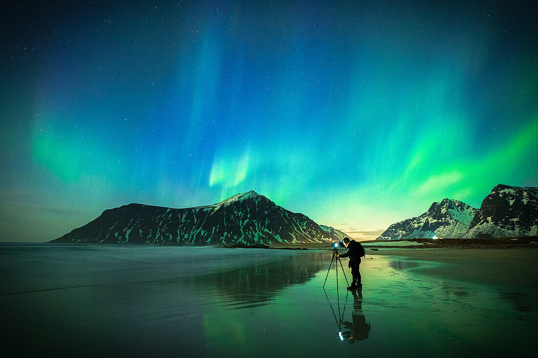 Person, die den hellen Himmel während der Aurora Borealis (Nordlichter) fotografiert, stehend am Skagsanden Strand, Lofoten Inseln, Norwegen, Skandinavien, Europa