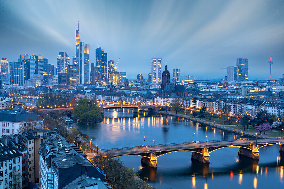 Langzeitbelichtung von Wolken in der Abenddämmerung über der beleuchteten Stadtsilhouette und der Ignatz-Bubis-Brücke, Frankfurt am Main, Hessen, Deutschland, Europa
