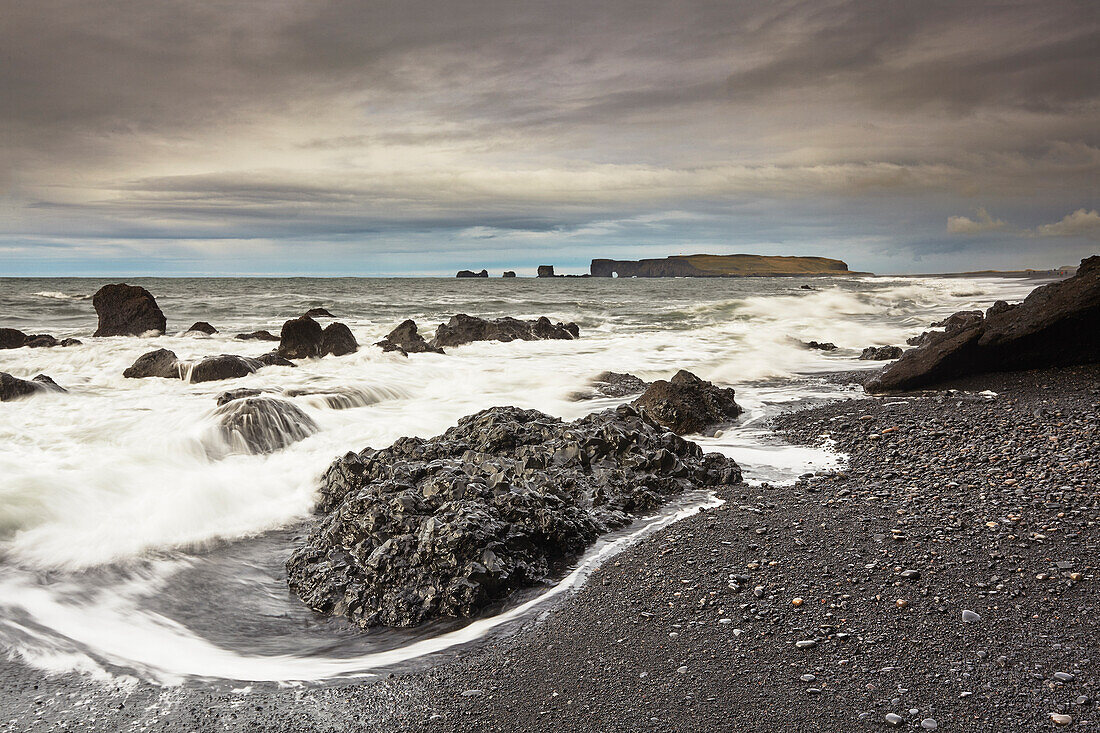 Lavafelsen bei Reynisfjara, mit der Insel Dyrholaey in der Ferne, in der Nähe von Vik, Südküste Islands, Polargebiete