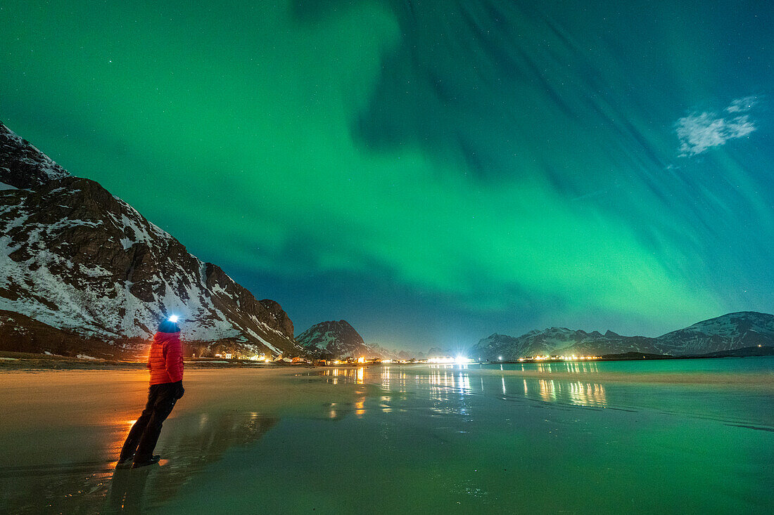 Wanderer mit Stirnlampe beobachtet die Aurora Borealis (Nordlichter) am Strand von Ramberg, Landkreis Nordland, Lofoten, Norwegen, Skandinavien, Europa