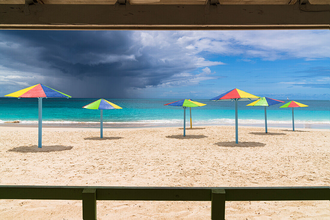 Mehrfarbig gestreifte Sonnenschirme am weißen Sandstrand unter Gewitterwolken, Antigua, Westindien, Karibik, Mittelamerika