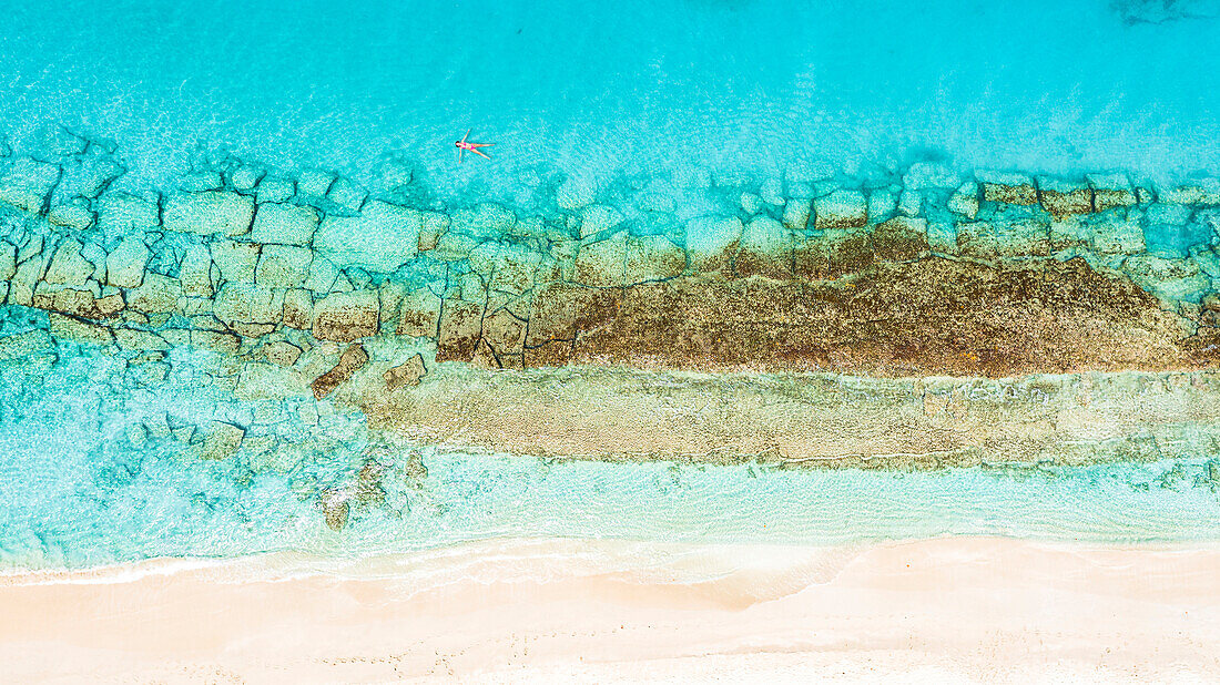 Luftaufnahme einer Frau, die auf dem kristallklaren Meer zwischen Korallenriff und weißem Sandstrand schwimmt, Antigua, Westindien, Karibik, Mittelamerika