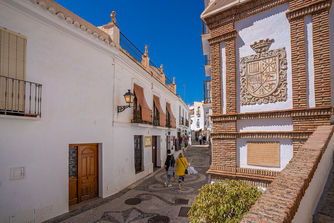 Blick auf weiß getünchte Häuser und Einkäufer in einer schmalen Straße, Frigiliana, Provinz Malaga, Andalusien, Spanien, Mittelmeer, Europa