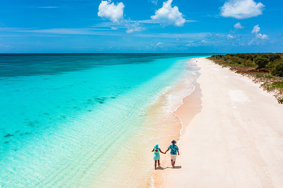Mann und Frau spazieren Hand in Hand an einem vom türkisfarbenen Meer umspülten Strand, Barbuda, Antigua und Barbuda, Westindische Inseln, Karibik, Mittelamerika