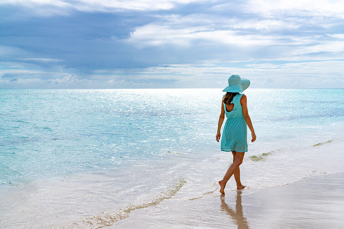Frau spaziert am weißen Sandstrand unter dem bewölkten Himmel bei Sonnenuntergang, Barbuda, Antigua und Barbuda, Westindien, Karibik, Mittelamerika