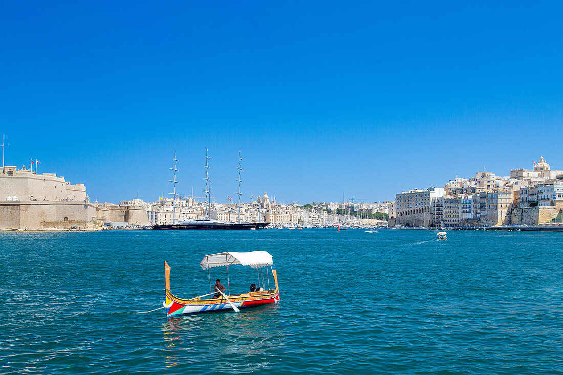 Traditionelle Fähre, die den Grand Harbour überquert, mit der Superyacht Malteser Falke im Hintergrund, Valletta, Malta, Mittelmeer, Europa