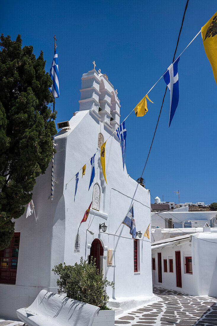 Kirche des Heiligen Georg und Fahnen in einer malerischen Straße in der Altstadt von Mykonos, Mykonos, Kykladen, Ägäisches Meer, Griechische Inseln, Griechenland, Europa