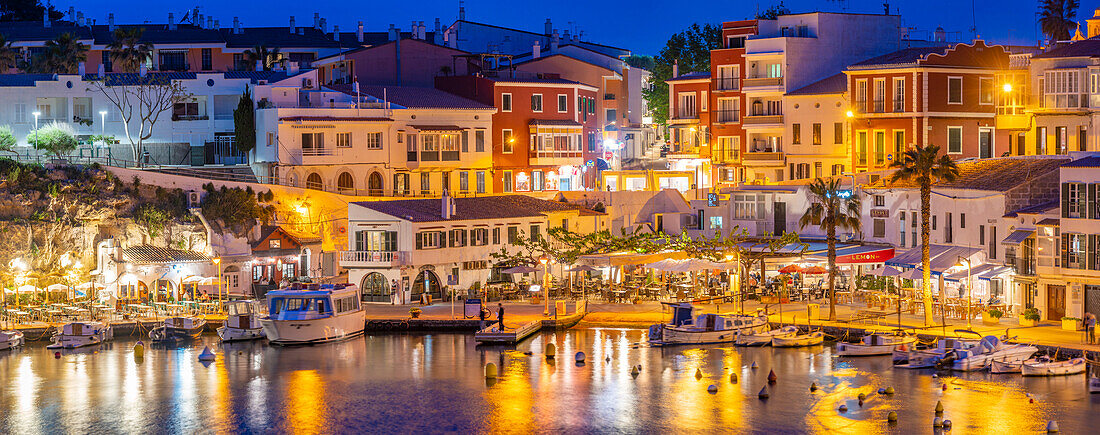 Blick auf Cafés, Restaurants und Boote im Hafen in der Abenddämmerung, Cales Fonts, Es Castell, Menorca, Balearische Inseln, Spanien, Mittelmeer, Europa