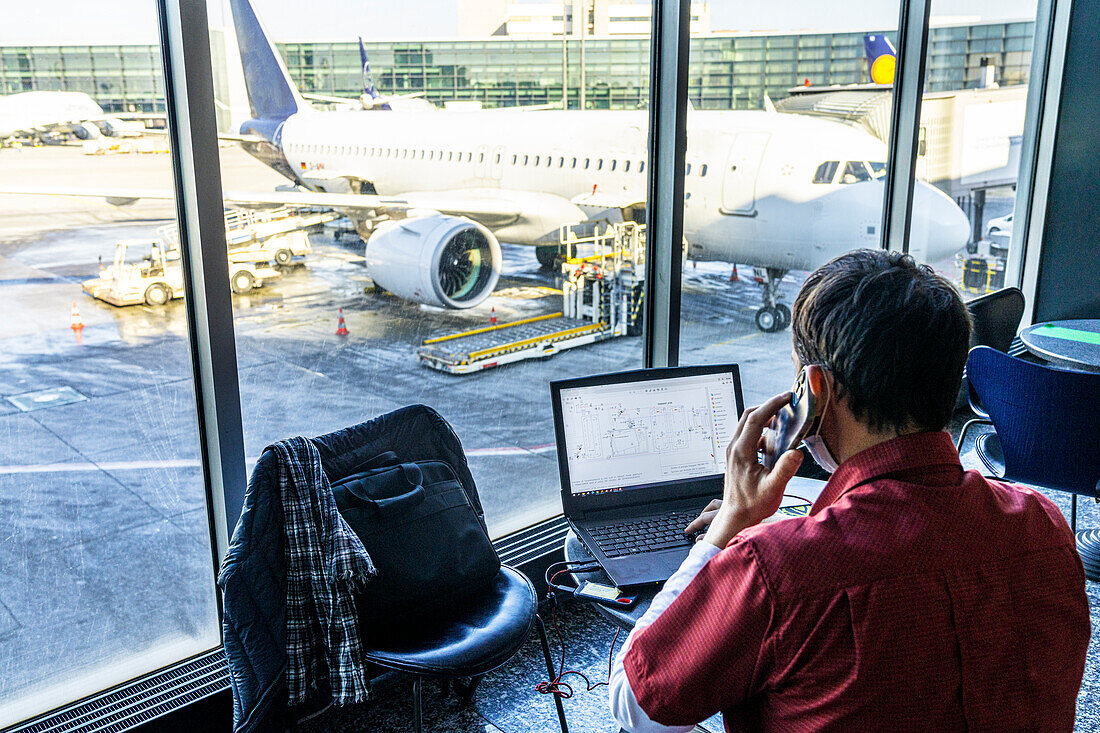 Rückansicht eines reifen Mannes mit Laptop und Smartphone beim Warten am Flughafen, Norwegen, Skandinavien, Europa
